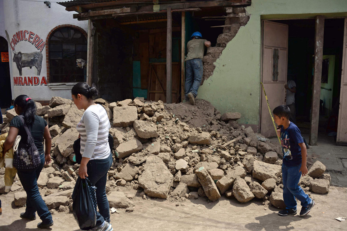 People walk by a house damaged by an earthquake, in San Pedro municipality, San Marcos departament, 240 km from Guatemala City, on July 7, 2014. A strong 6.9-magnitude earthquake rocked parts of southern Mexico and Guatemala on Monday, killing at least two people and injuring more than 40 others. The US Geological Survey said the quake -- initially measured at a magnitude of 7.1 -- struck the Pacific coast of Mexico's Chiapas state at about 1124 GMT at a depth of 60 km. The epicenter was located just two km from the Mexican town of Puerto Madero, and 200 km from Guatemala City. AFP PHOTO / Johan ORDONEZ
